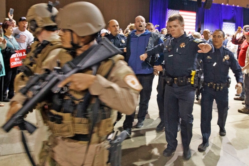 A man is escorted by law enforcement officers moments after Donald Trump was rushed off stage by Secret Service agents.